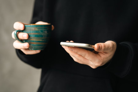 Smartphone and a cup of coffee in the hands of a man close-up.の写真素材