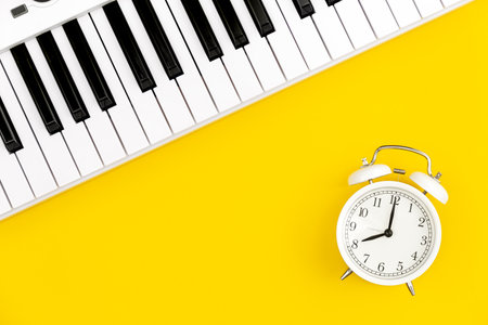 White alarm clock and piano on a yellow background, top view, copy space.の写真素材