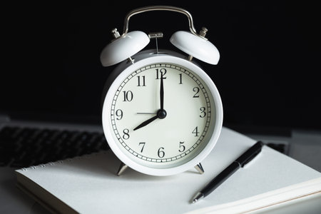 Alarm clock, notepad and laptop at the workplace, close-up.の写真素材