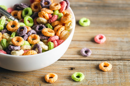 Colored breakfast cereals in a bowl on a wooden background, close up.