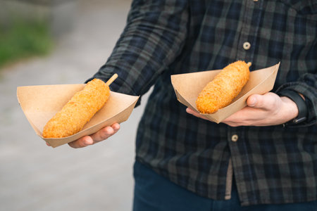 Hand holding a tasty corn dogs on a blurred city background.の写真素材