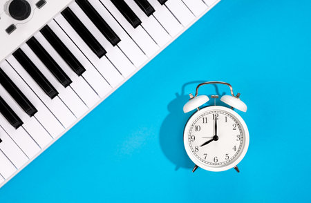 White alarm clock and piano on a blue background, top view.の写真素材