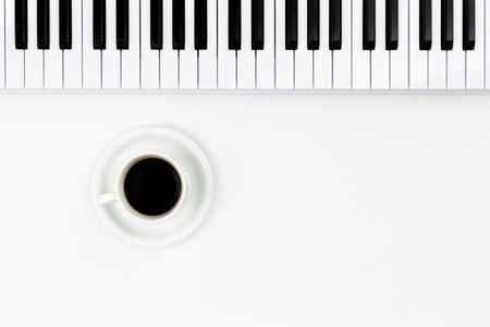 Musical keyboard and a cup of coffee on a white background, top view.
