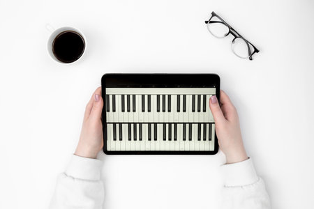 Digital tablet with piano keys in female hands on a white background, top view.の写真素材
