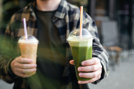 A man outdoors holds a plastic glass with a green banana and mint smoothie.