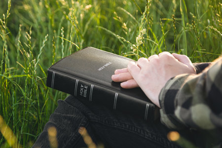 Man praying on the holy Bible in a field during sunset, close up.の写真素材