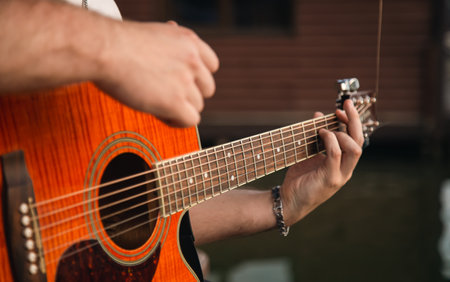 A man plays the guitar, sitting on a wooden pier near the lake.の写真素材