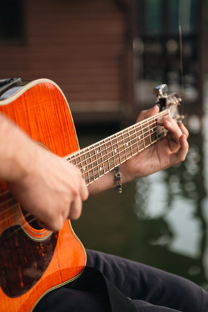 A man plays the guitar, sitting on a wooden pier near the lake.の写真素材