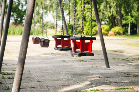 Red empty chain swing in playground on a blurred background, close up.