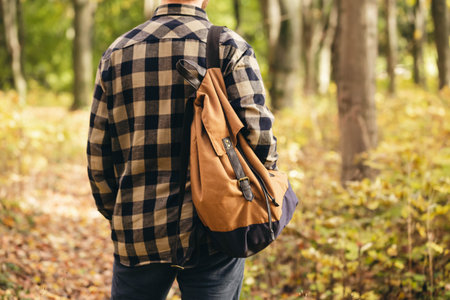 Traveler with a backpack is walking on an road along autumn forest.