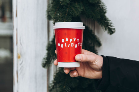 A man holds a red cup with the inscription Happy Holidays, close-up.の写真素材