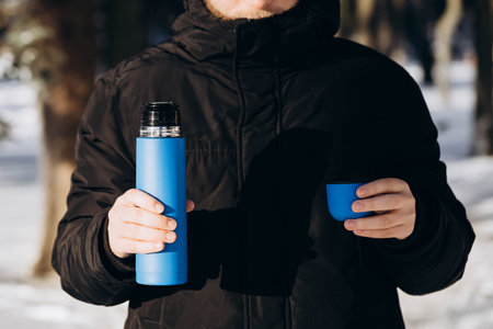 A flask in the hands of a man in the winter forest. Thermal cup in male hands.の写真素材