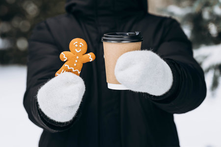 Smiling gingerbread man and paper cup of coffee in hands on blurred background.