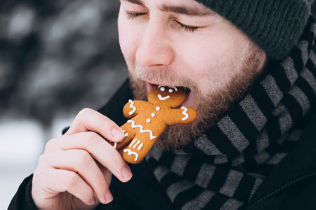 A young man in a hat eats a gingerbread man, close-up.の写真素材
