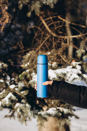 A blue flask in male hand against the backdrop of a winter forest.