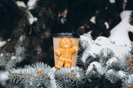 Paper cup and gingerbread man on a snowy Christmas tree branch, copy space.