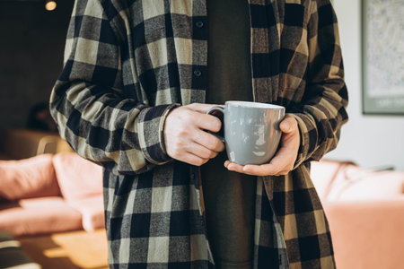 A gray cup in the hands of a man in a checkered shirt in a modern office.の写真素材