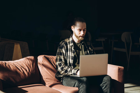 A bearded young man works in a cafe with a laptop remotely.の写真素材