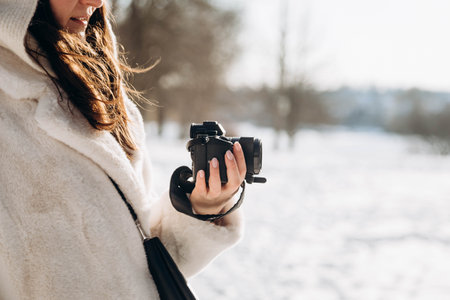 A woman holds a camera in her hand outdoors in winter.の写真素材