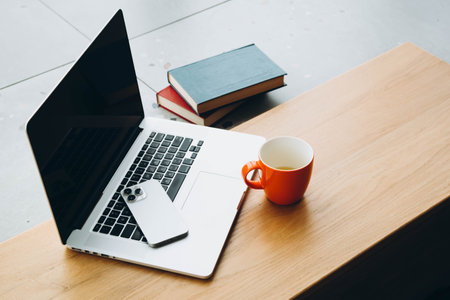 Laptop, smartphone, cup of tea and books on a wooden tabletop.の写真素材