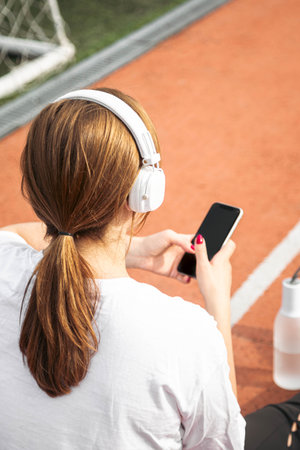 A woman with headphones uses a smartphone on a treadmill at the stadium.の写真素材