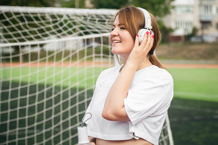 Female athlete with white headphones at the stadium near the football goal.の写真素材