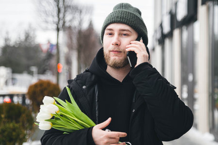 A young man is talking on the phone and holding a bouquet of tulips outside.の写真素材