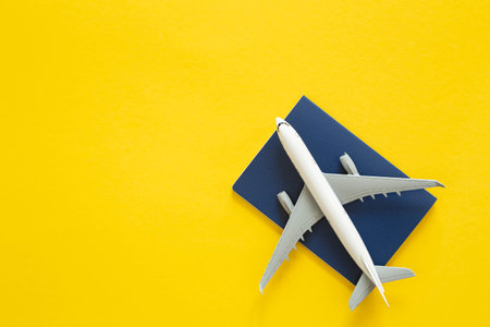 Toy passenger plane and passport on yellow background isolated, top view.の写真素材