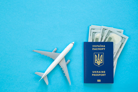Ukrainian biometric passport, money and airplane on a blue background, top view.の写真素材