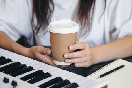 A cup of coffee in the hands of a female keyboard player at the workplace.の写真素材