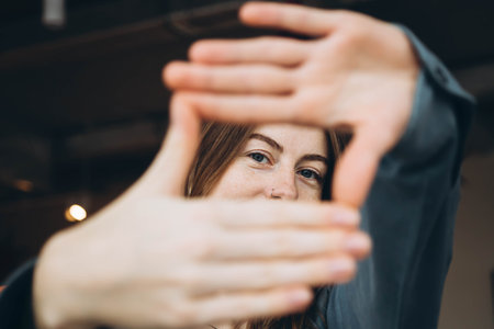 A young woman with blue eyes in a blue shirt makes a frame from her fingers.の写真素材