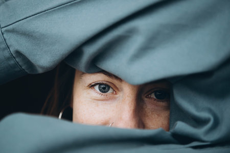 A young woman with blue eyes and freckles hides her face in a blue shirt.の写真素材