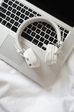 White headphones and laptop on white sheets in bed, top view.の写真素材