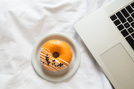 Orange donut and laptop in white bed close up.の写真素材