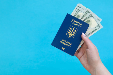 Biometric Ukrainian passport and money in a hand on a blue background isolated.