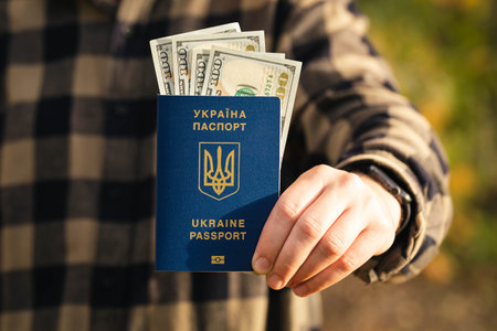 A man holds a biometric Ukrainian passport and dollar bills in his hand.の写真素材