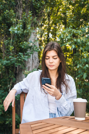A young woman uses a smartphone while sitting outside on the terrace.の写真素材