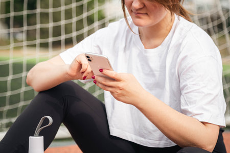 A woman uses a smartphone while sitting on a treadmill at the stadium.の写真素材