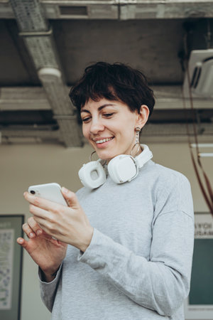 Stylish woman with short hair with white headphones uses a smartphone.