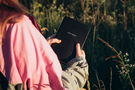 Christian girl holds bible in her hands in a field during sunset, copy space.