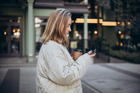 A young woman uses a smartphone and drinks coffee on the way to work.の写真素材