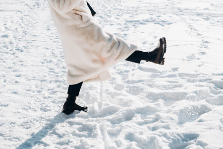 A woman in a white fur coat and winter boots kicks up snow with her feet.の写真素材