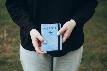 A passport in a blue cover in the hands of a woman with a blue manicure.の写真素材