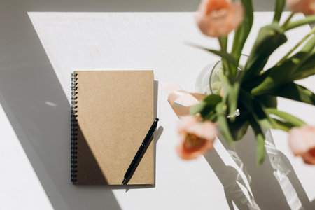 Recycled notebook and tulip flowers on white desk background, flat lay.