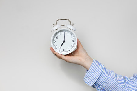 Woman hand holding white alarm clock on white background. Seven oclock.の写真素材