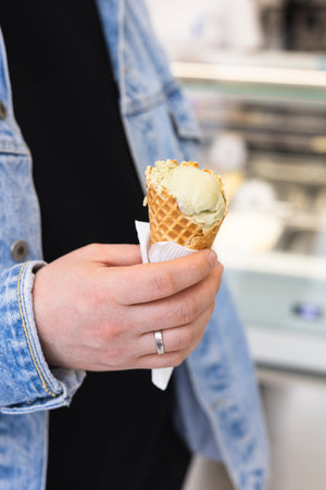 Male hand holding ice cream cone in waffle cup at ice cream shop, close-up view.の写真素材