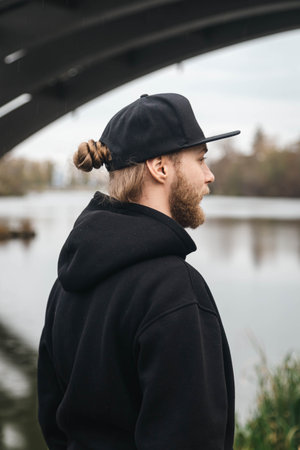 A young man in a black cap stands by the river and looks into the distance.