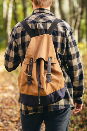 Traveler with a backpack is walking on an road along autumn forest.