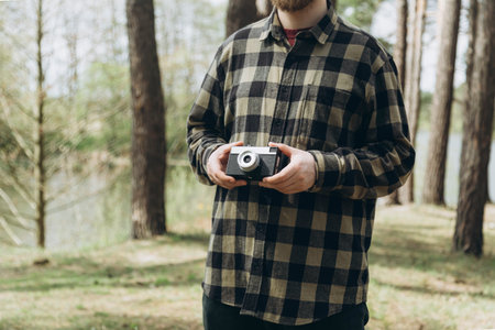 A male photographer holds a film camera, takes photographs in the forest.