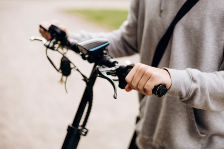 Close-up of a teenage boy hands gripping an electric scooter outdoors.の写真素材
